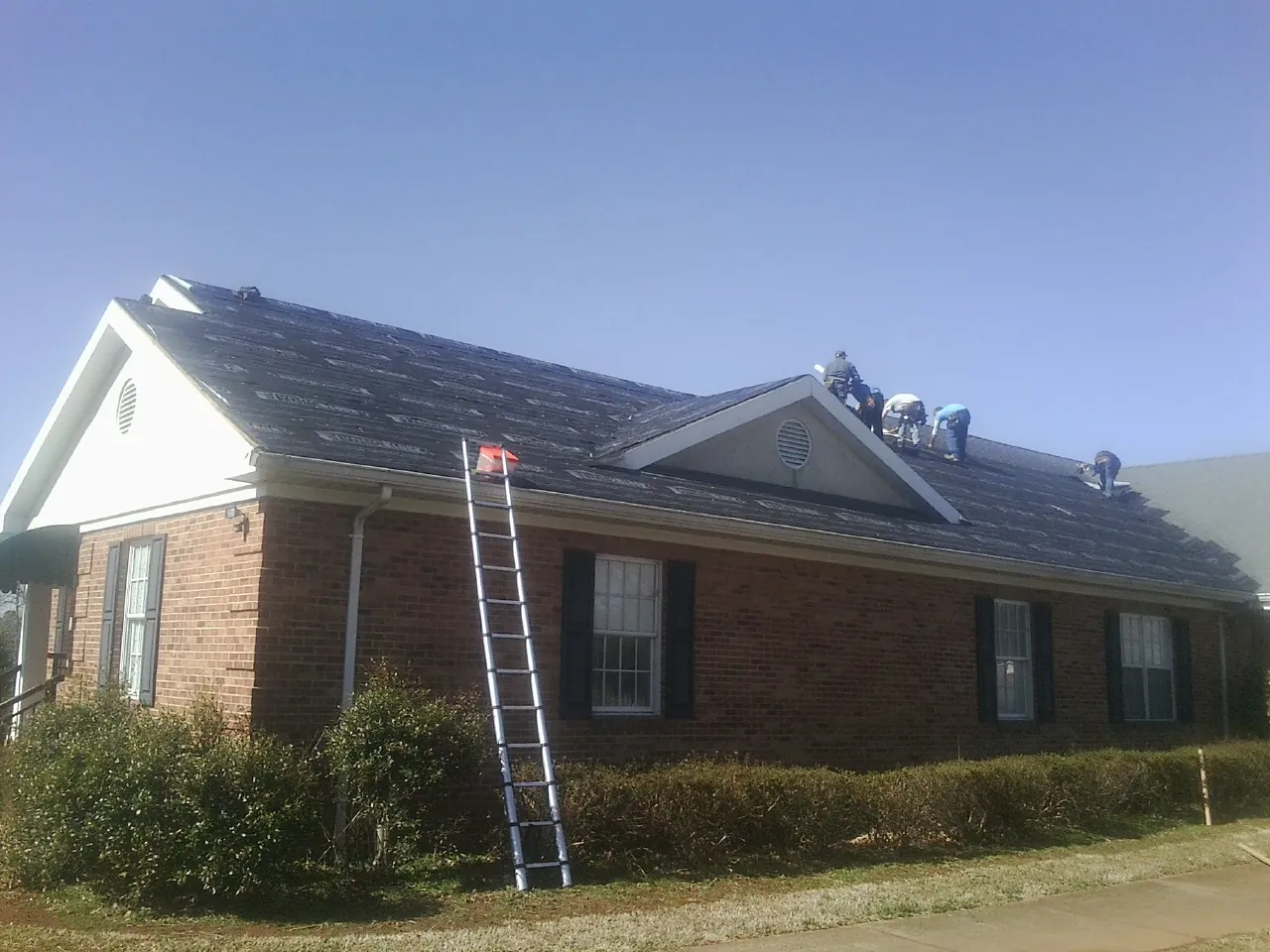 Crew tearing shingles off a brick ranch roof with a ladder set — Emergency Roof Repair work by our crew in Freeland