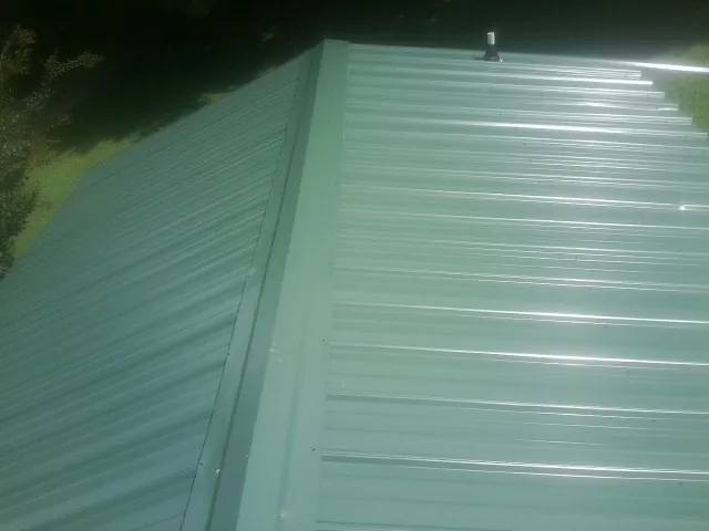 New green metal panels meeting at the ridge of a roof — Flat Roof Repair work by our crew in Freeland