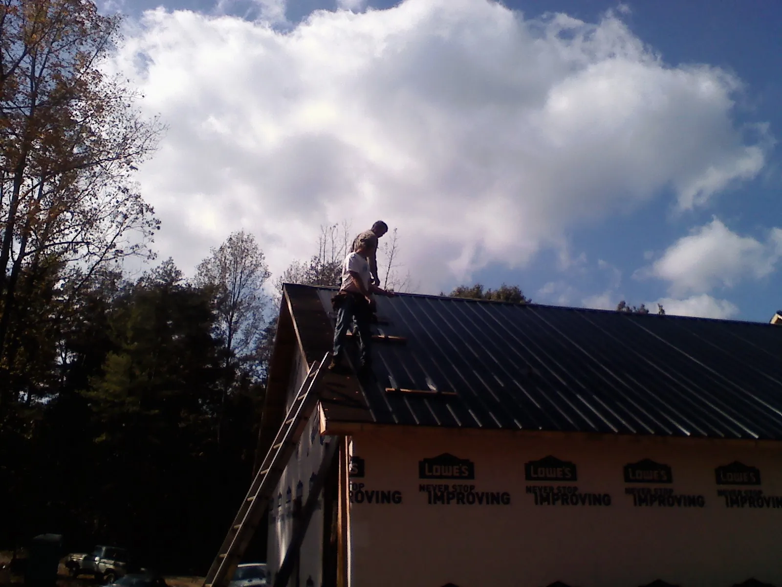 Roofer fastening dark metal panels high against a cloudy sky, from a Roof Inspection job in Freeland